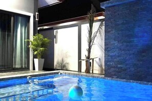 Una piscina interior con agua cristalina, una pelota flotando y una planta en maceta.