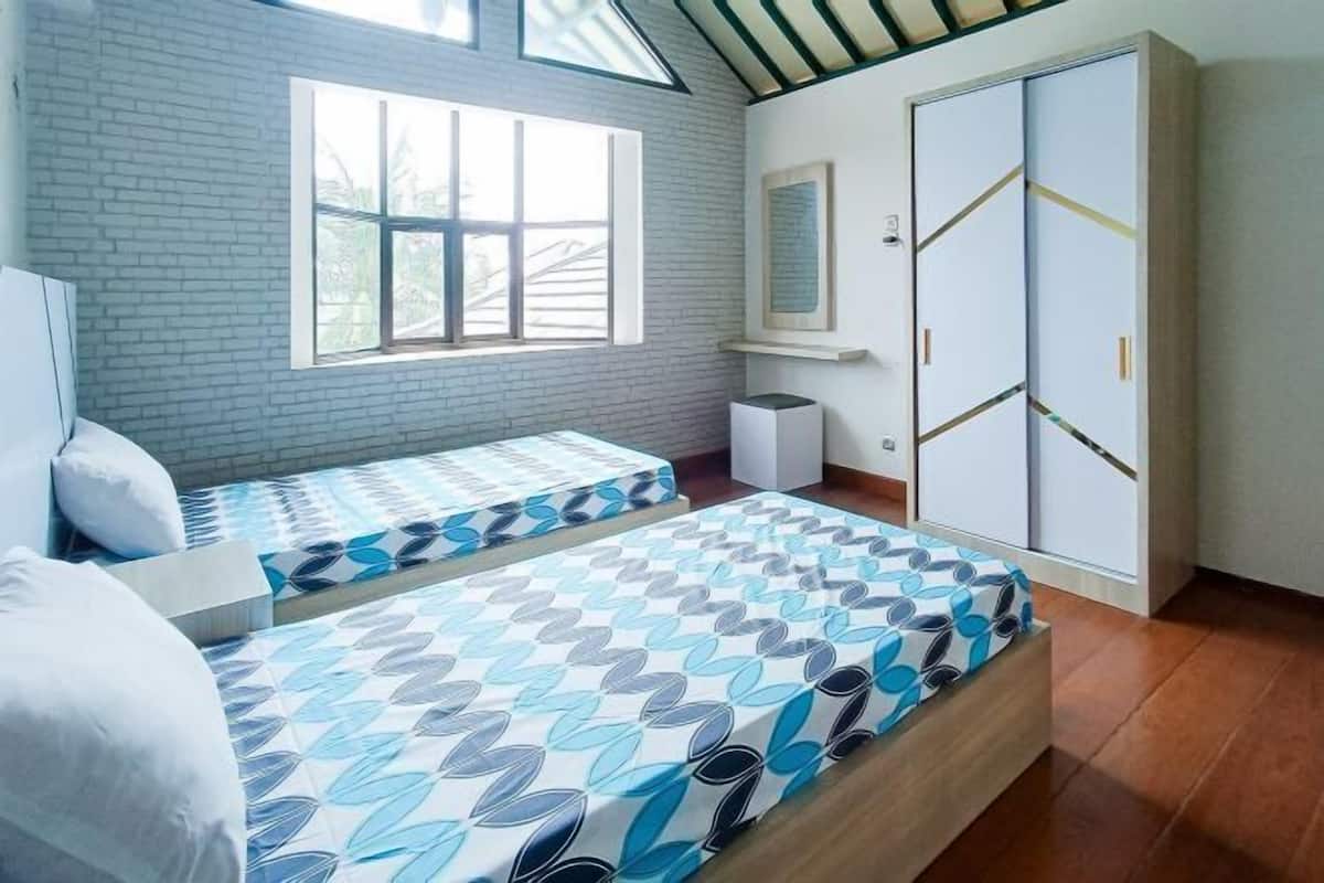 A bedroom with two beds, a window, a wardrobe, and a small bedside table.