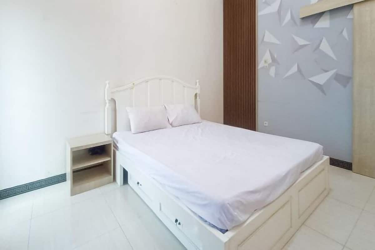 A single-bed room with a white headboard, a bedside table with a shelf, and a wall with geometric patterns.