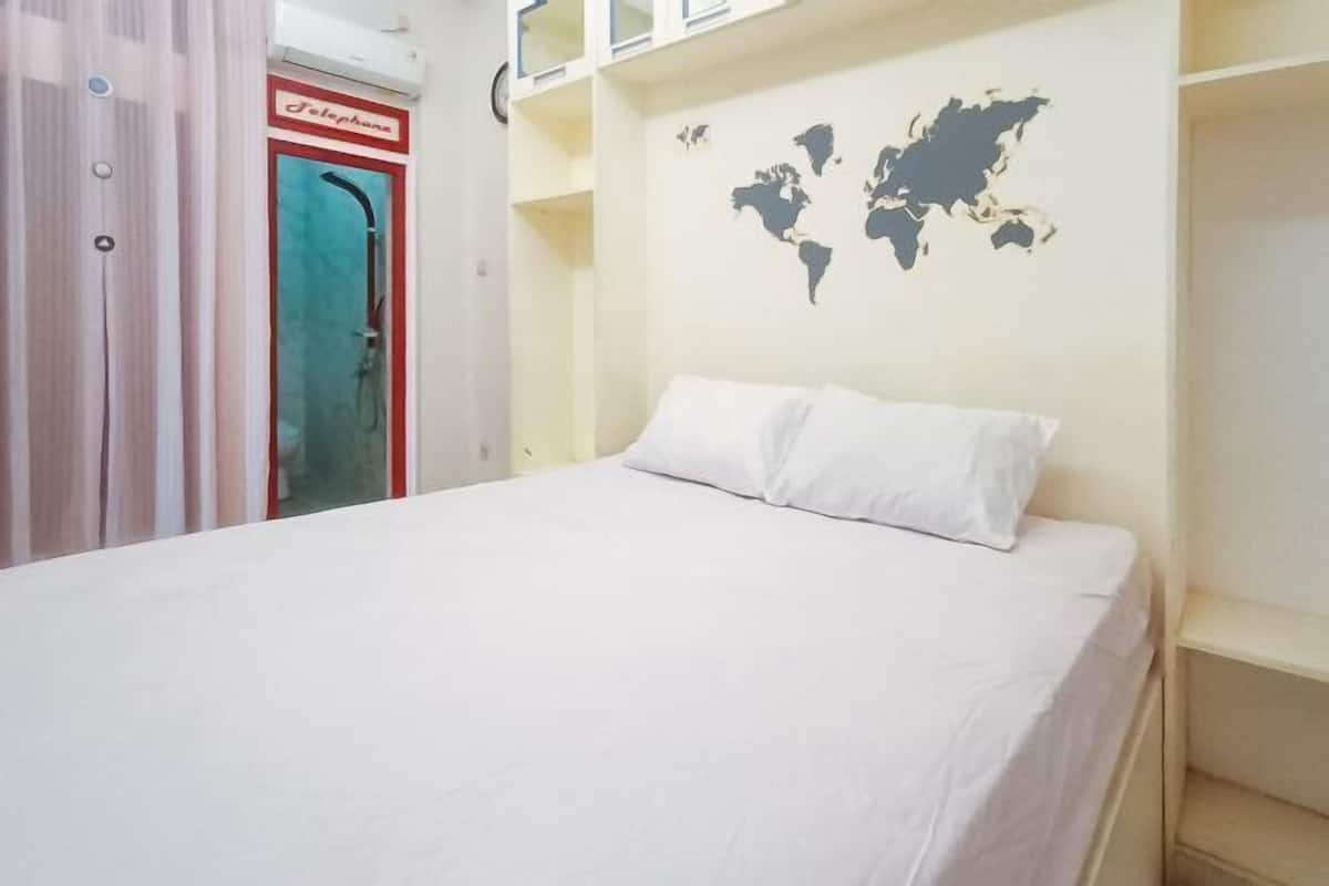 A hotel room with a bed, a world map on the wall, and a shower area with a red sign.