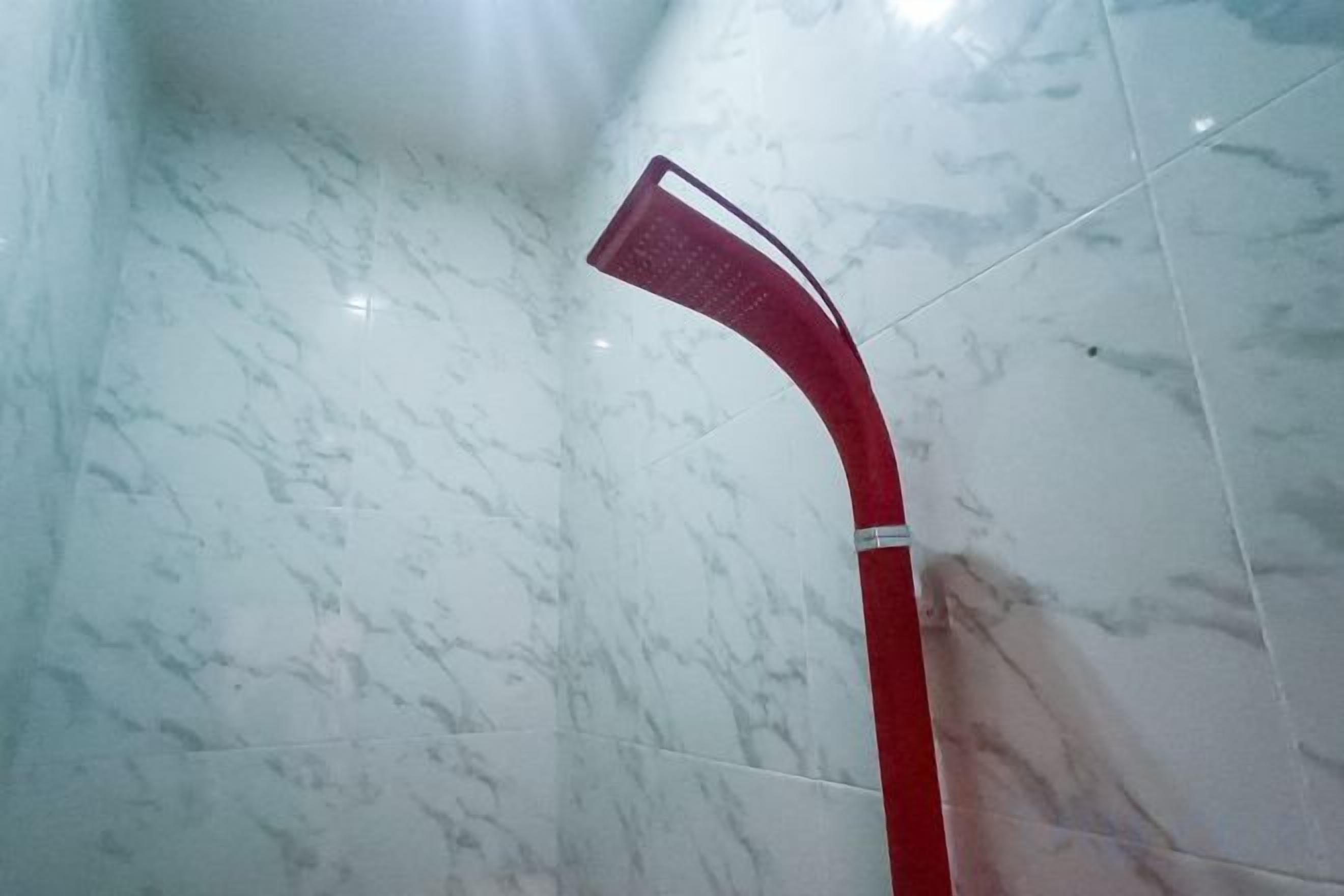 Une pomme de douche rouge dans une salle de bain carrelée de marbre.