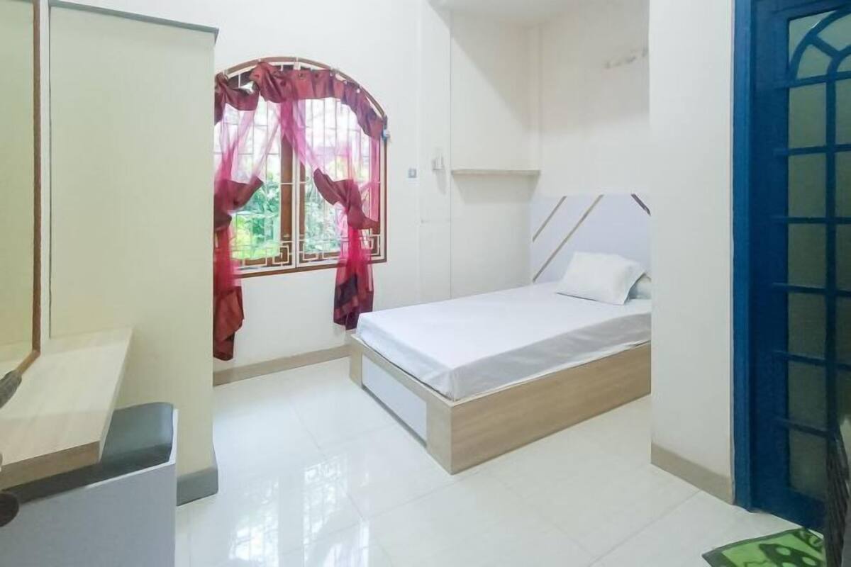A bedroom with a bed, a window with curtains, a white door, and a blue door.