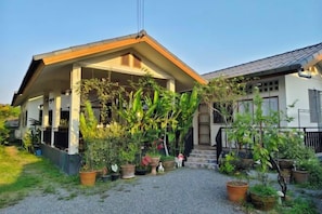 A two-story house with a covered porch, surrounded by potted plants and a gravel driveway. - Chiang Mai Downtown Privacy Home (Chiang Mai)