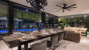 A modern dining area with a long table set for a meal, surrounded by comfortable seating. - Villa Balimu Seminyak (Bali)