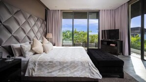 A modern bedroom with a large bed, a TV, and a balcony with a view of greenery. - Villa Balimu Seminyak (Bali)
