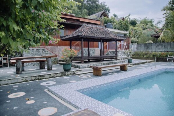 A swimming pool with a tiled deck, benches, and a gazebo. - RedDoorz @ Villa Bukit Senyum Lombok (South Kuripan)