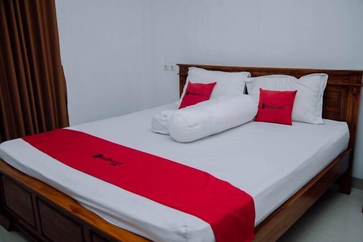 A neatly made bed with white and red bedding, a wooden headboard, and a red throw blanket.