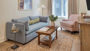 Ein modernes Wohnzimmer mit einem grauen Sofa, einem Holztisch, einem gestreiften Sessel und einem großen Fenster mit Vorhängen.
