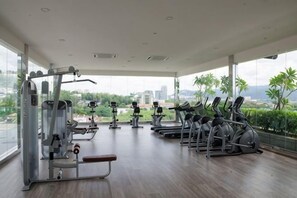 Un gimnasio con máquinas de cardio y equipo de pesas, ventanas amplias y vista a un paisaje urbano.