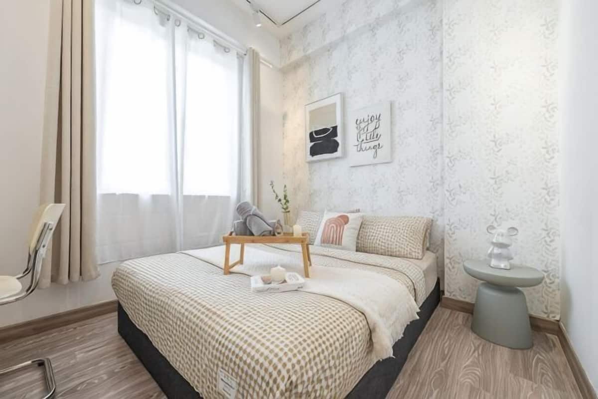 Een slaapkamer met een bed, nachtkastje, stoel en een raam met gordijnen.