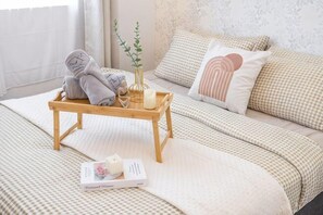 Une chambre à coucher bien rangée, avec un lit, des oreillers, une table de chevet sur laquelle se trouve une pile de serviettes, un vase avec une plante et un livre.