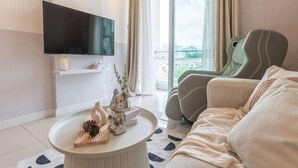 Ett modernt vardagsrum med en platt-TV, ett runt soffbord med dekorativa föremål, en soffa och utsikt över staden genom stora fönster.