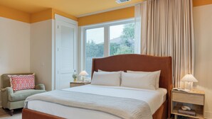 Un dormitorio con una cama grande, una mesita de noche con lámpara, una silla y una ventana con cortinas.