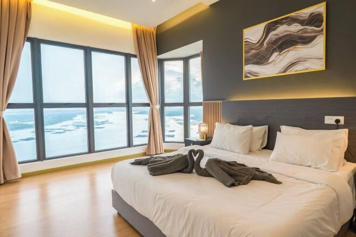 Quarto de hotel com uma cama grande, vista para o oceano através de janelas do chão ao teto e um quadro abstrato moderno na parede.