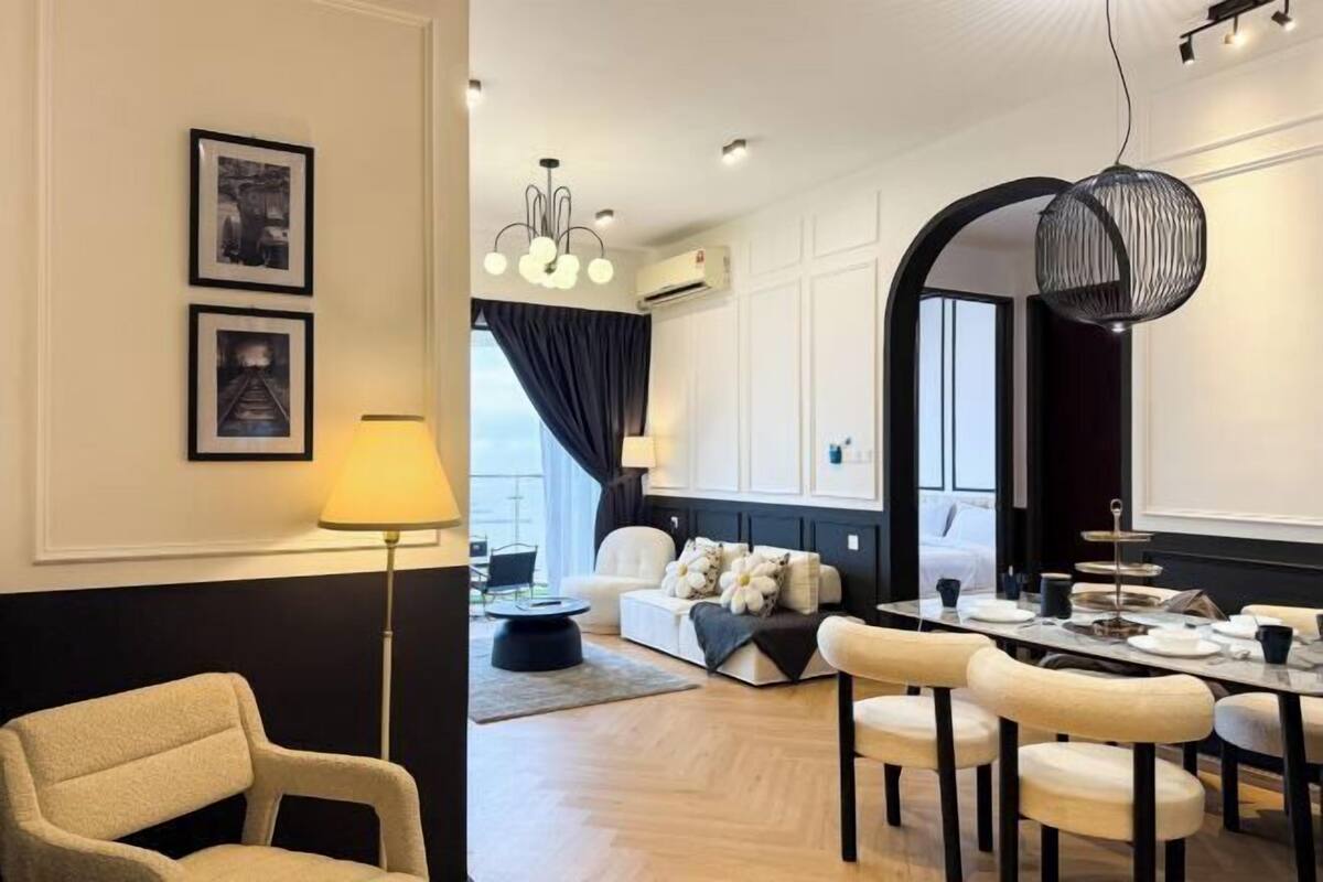 Quarto de hotel moderno com área de jantar, sofá, luminária e um espelho grande.