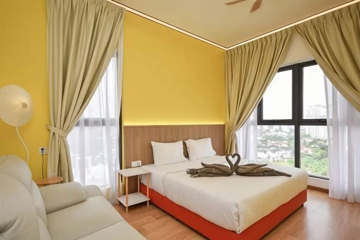 Quarto de hotel com cama, escrivaninha, cadeira e uma janela grande.
