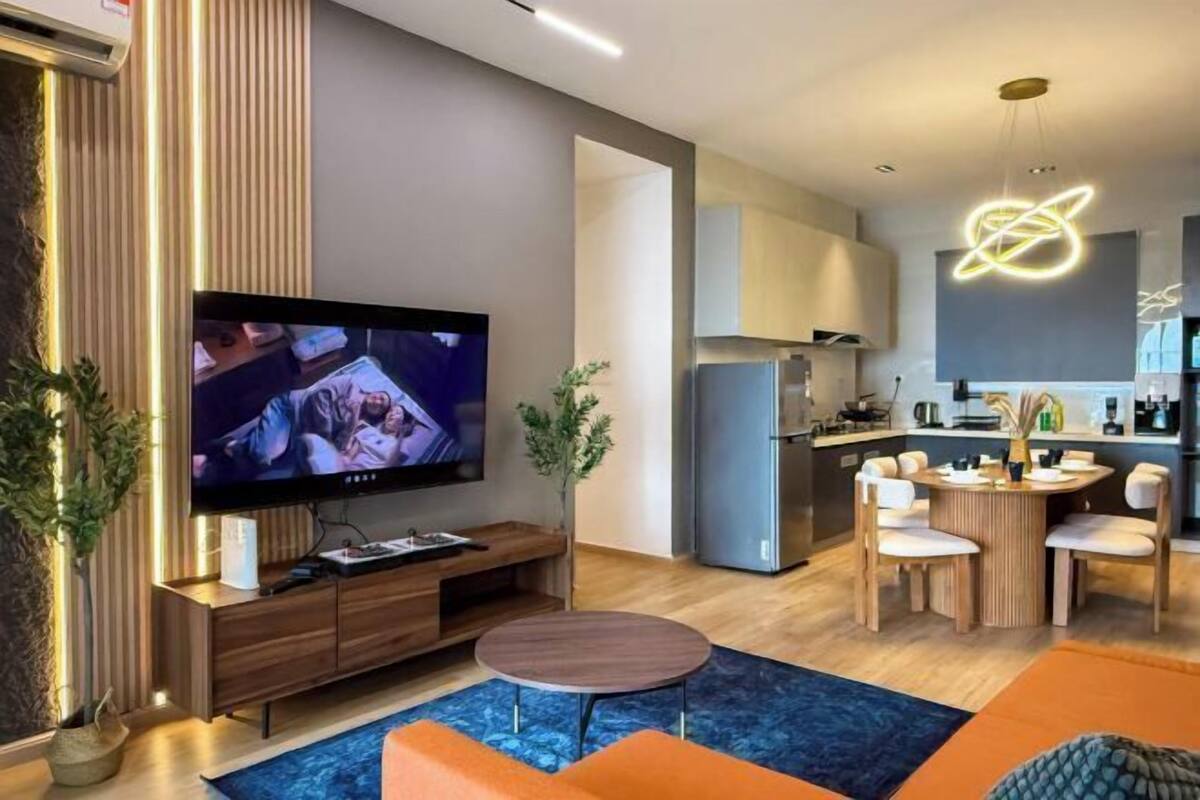Uma sala de estar moderna com uma televisão de tela plana, um rack de madeira, uma mesa de centro redonda e sofás laranja.