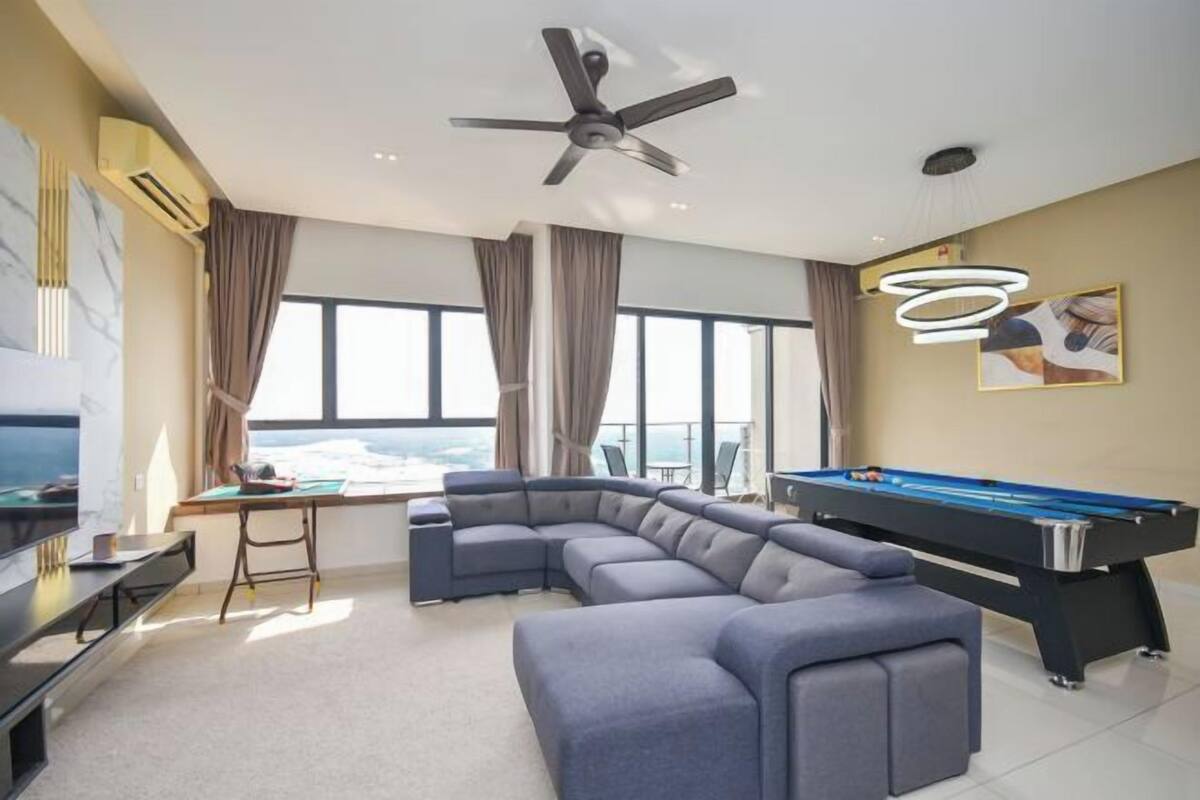 Uma sala de estar moderna com mesa de bilhar, sofá modular, ventilador de teto e uma grande janela com vista.