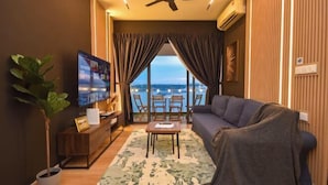 Una sala de estar con sofá, televisor y vista al mar a través de amplias ventanas.