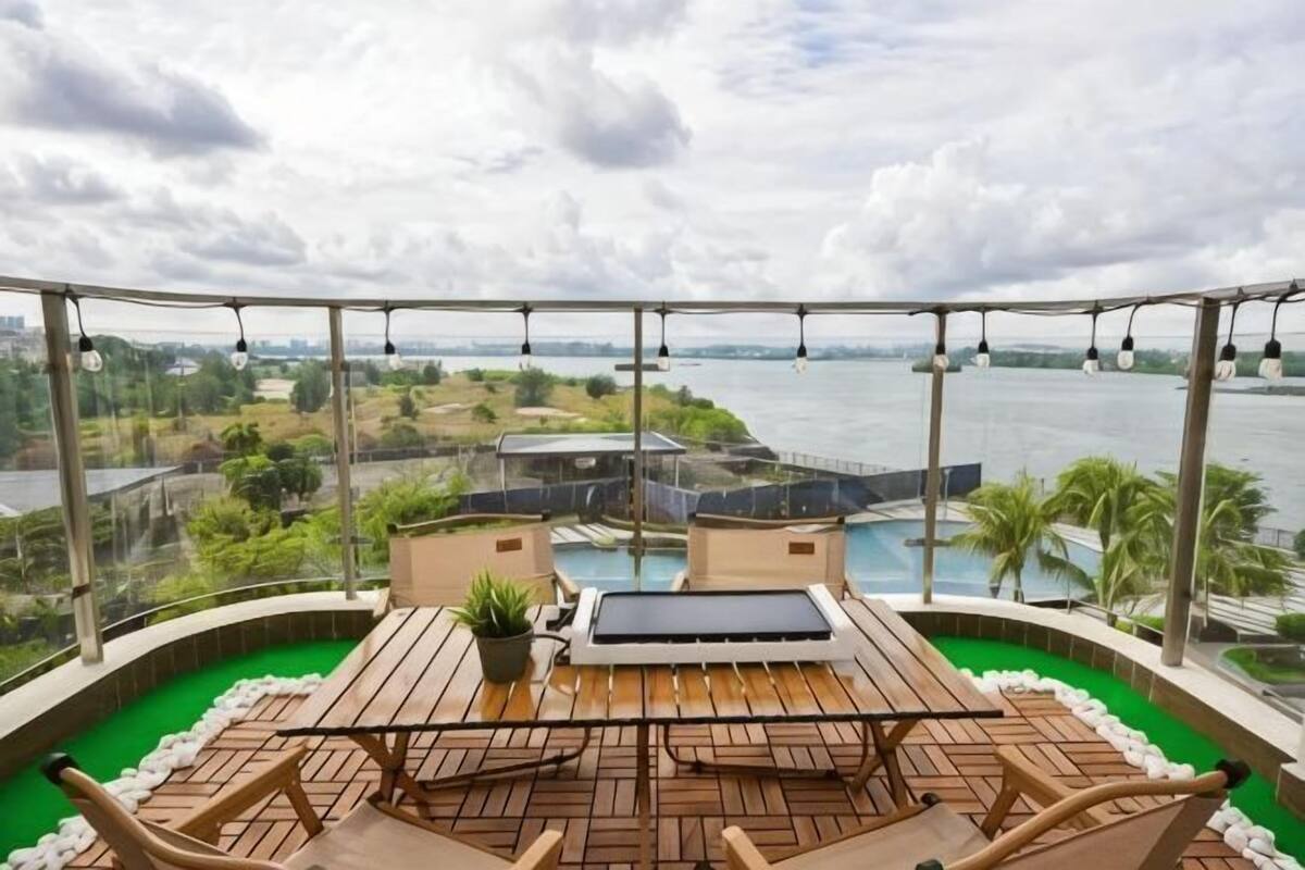 Terraço no telhado com vista para um corpo de água, uma piscina e área de refeições com mesa e cadeiras.