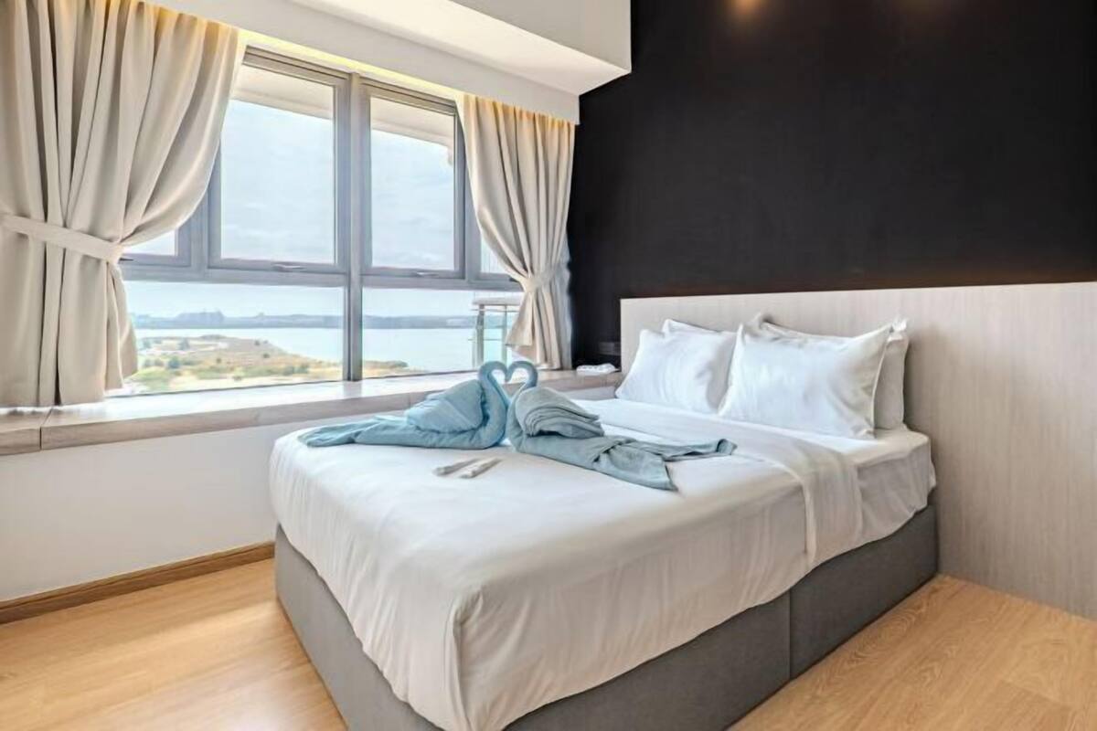 Quarto de hotel com uma cama grande, vista para a água e janela com cortinas.