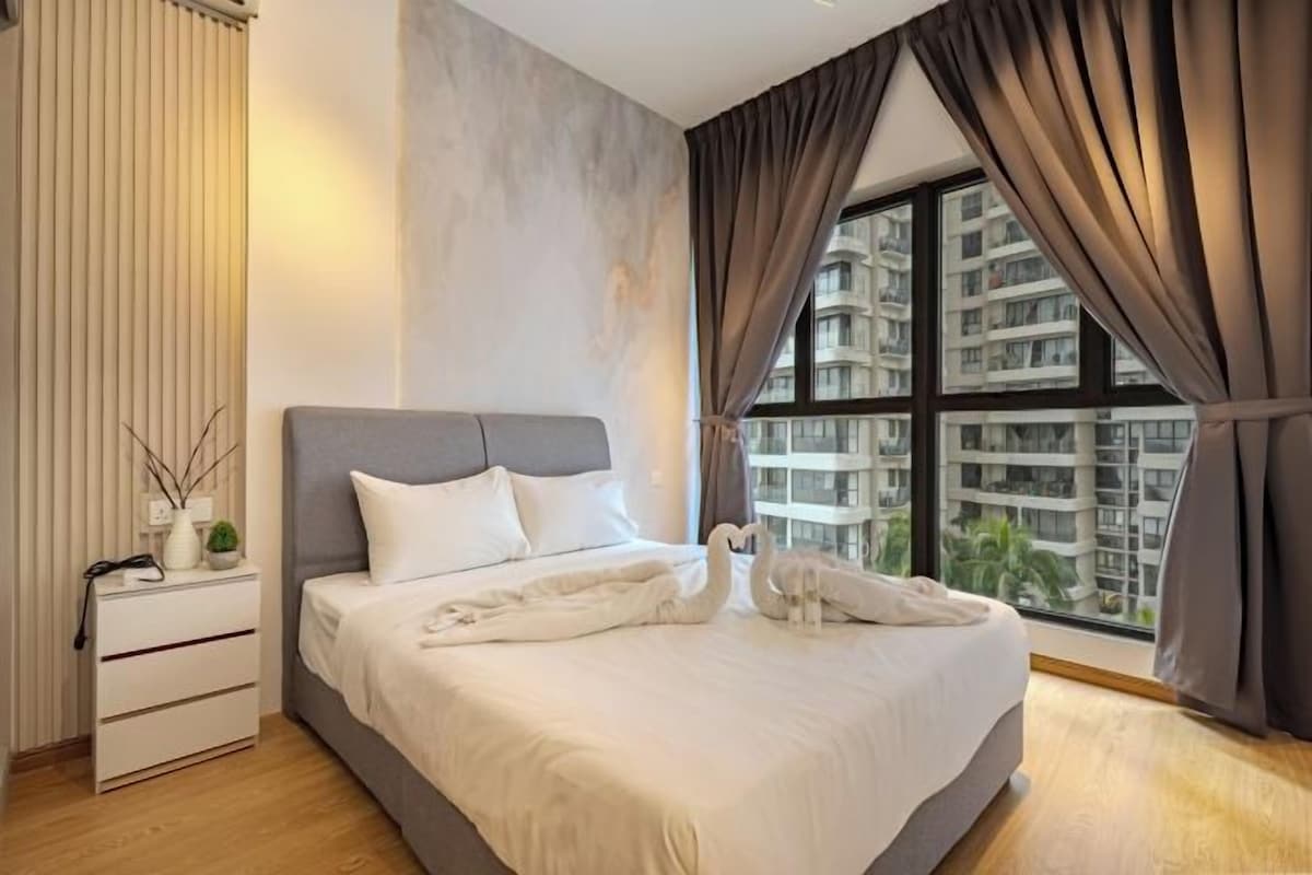 Een moderne slaapkamer met een groot bed, een nachtkastje, een raam met gordijnen en uitzicht op gebouwen.