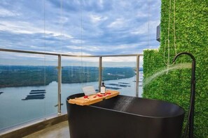 A modern bathroom with a black bathtub, a wooden tray with rose petals, and a bottle. - Country Garden Seaview Suite by Nest Home at Danga Bay (Johor Bahru)