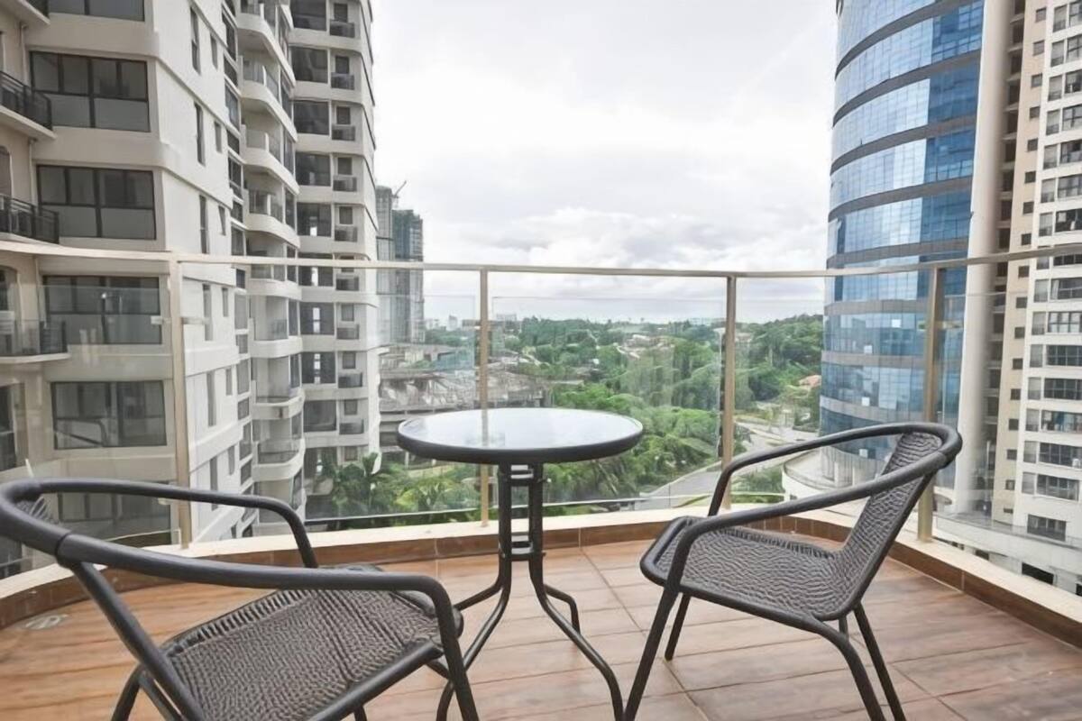 A balcony with a round table and two chairs, overlooking a cityscape with high-rise buildings.
