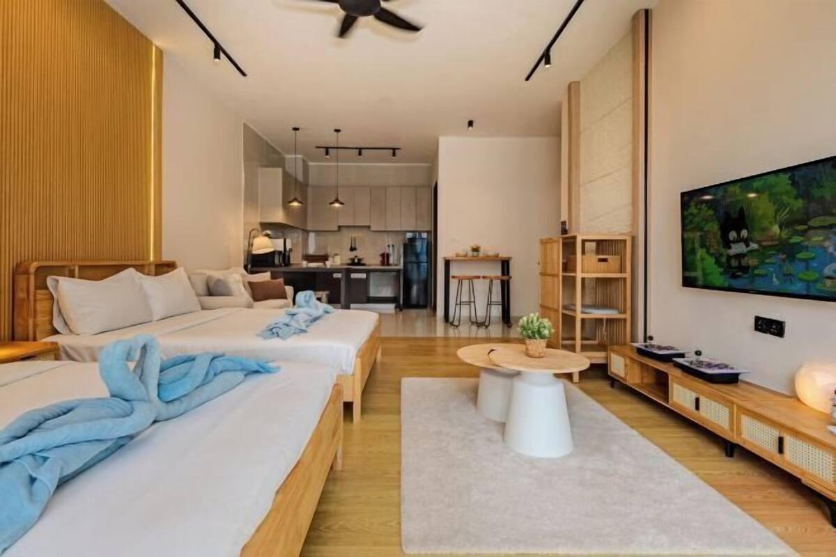 Quarto de hotel moderno com duas camas, área de refeições, cozinha e televisão na parede.