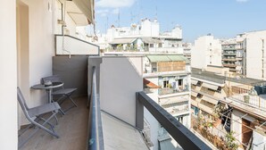 Un balcon avec une table et des chaises, donnant sur une zone urbaine densément peuplée, avec différents bâtiments et balcons.