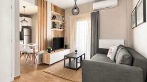 Un salon moderne avec un canapé gris, un meuble de rangement en bois, un coin repas avec des chaises blanches et une cuisine en arrière-plan.