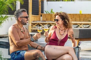 Two people sitting by a poolside, holding drinks, with a wooden deck and outdoor furniture in the background. - La Belle Vie - Boutique Hotel Adults Only (Koh Phangan)