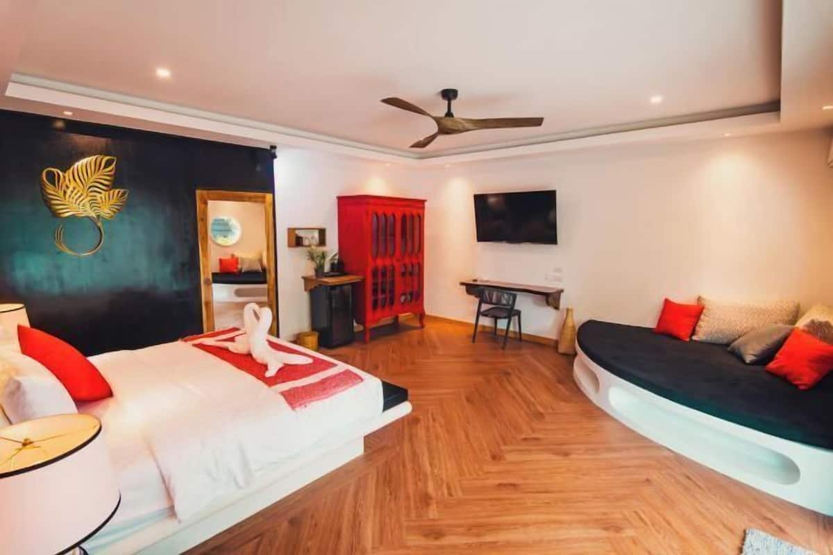 Ein Hotelzimmer mit Bett, Sofa, Schreibtisch, Fernseher und Deckenventilator.