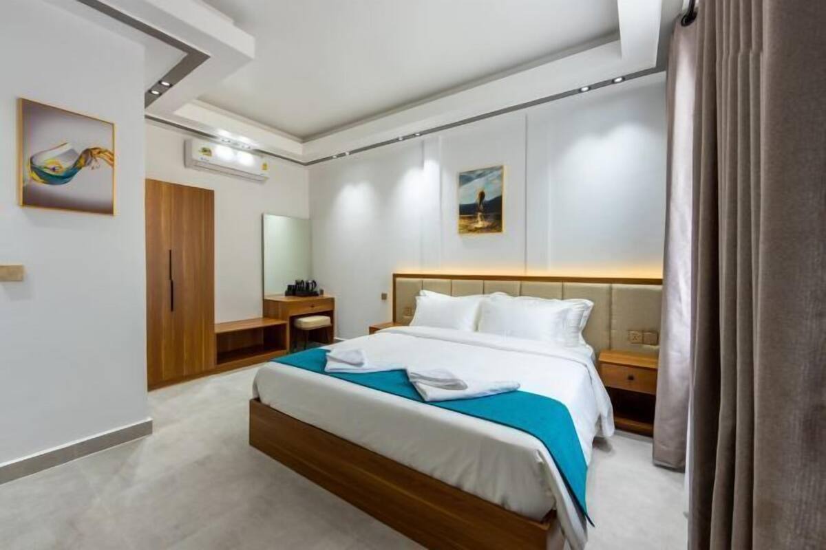 A hotel room with a bed, bedside tables, a wardrobe, a mirror, and artwork on the walls.
