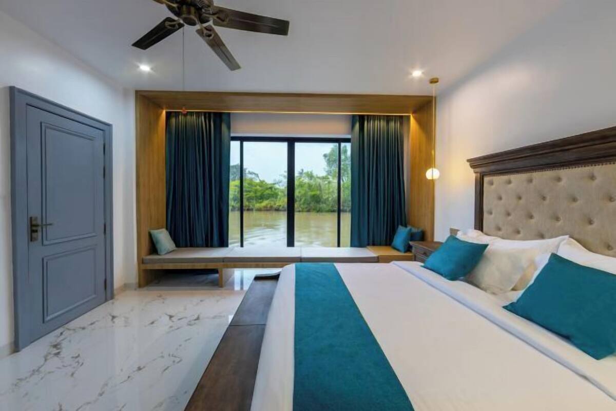 A bedroom with a bed, a bench, a ceiling fan, and a view of greenery outside.