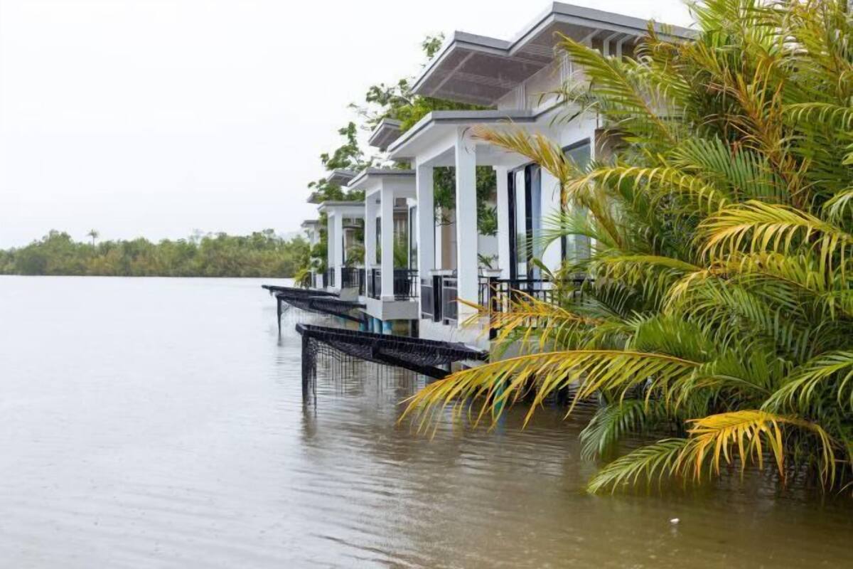 A waterfront property with a series of white buildings supported by columns, connected by a covered walkway.