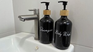 Un lavabo de salle de bain avec deux flacons noirs étiquetés « Shampoing » et « Gel douche », dotés de distributeurs à pompe en bois.