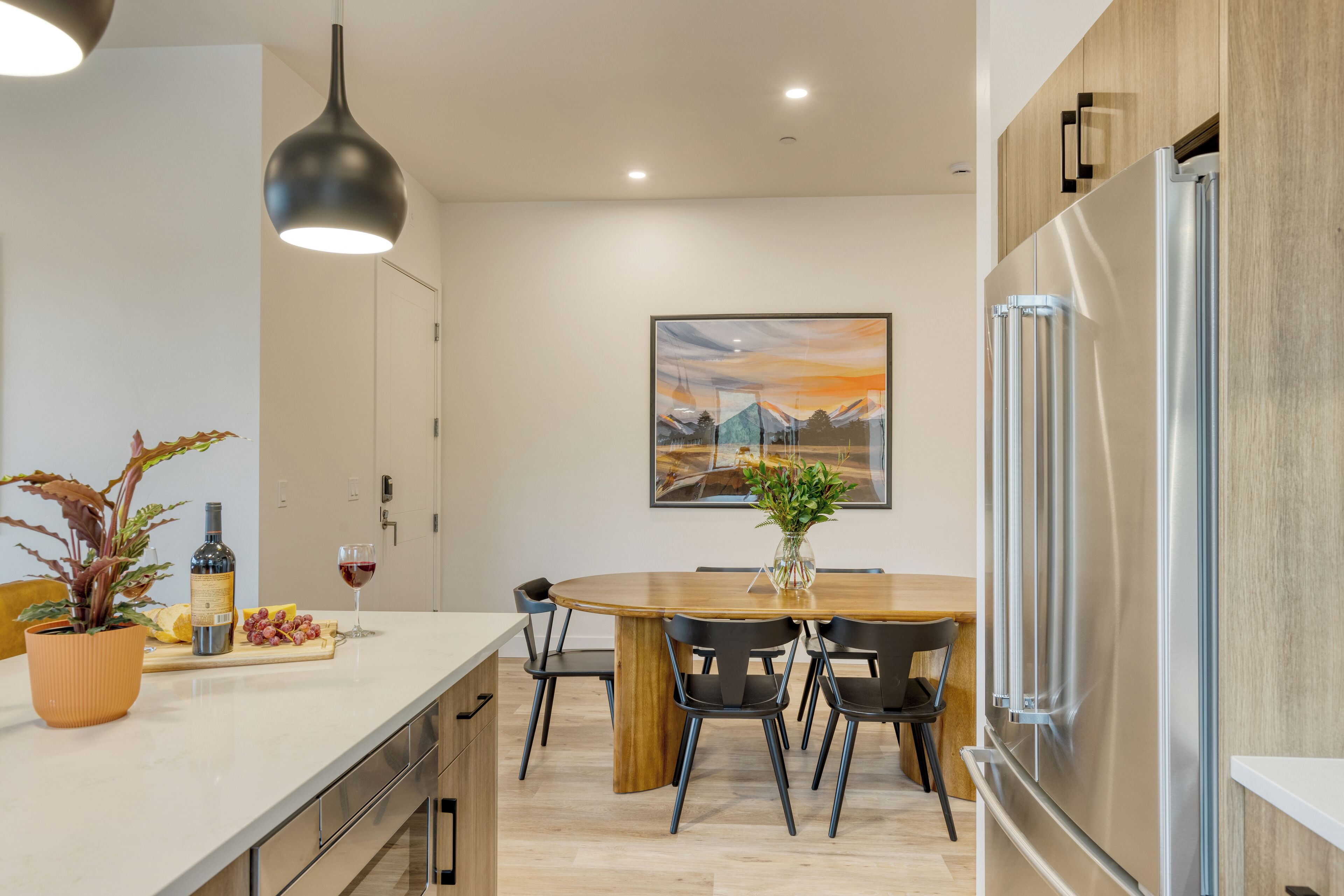 Una cocina moderna con una mesa de comedor de madera, sillas negras, un refrigerador de acero inoxidable y una planta en maceta.