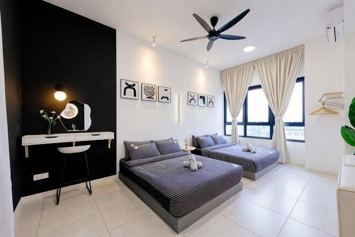 Une chambre moderne équipée d’un bureau, de deux lits, d’un ventilateur de plafond et de grandes fenêtres.