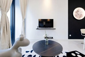 Een moderne woonkamer met een ronde tafel, een flatscreen tv aan de muur en een decoratieve lamp in de vorm van een maan.