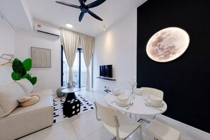 Un salon moderne avec un canapé blanc, une table à manger avec des chaises, un ventilateur de plafond et un téléviseur fixé au mur.