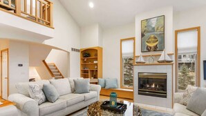 A spacious living room with a high ceiling, a fireplace, a staircase, and a bookshelf. - Viewhouse | Private Beach Access | Walkable | EV (Spring Lake)