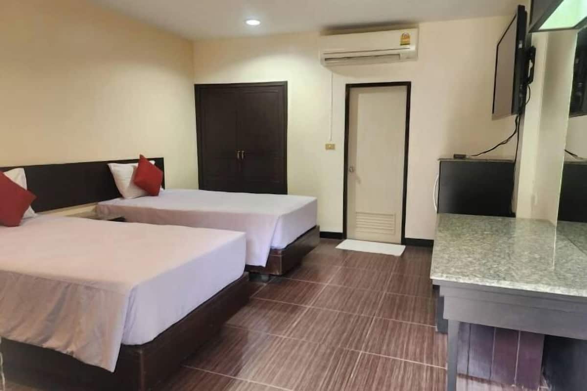 A hotel room with two beds, a desk, an air conditioning unit, and a television.