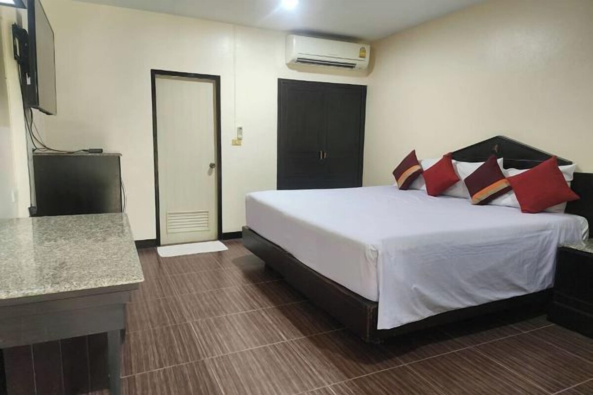 A hotel room with a bed, a desk, an air conditioner, a wardrobe, and a door.