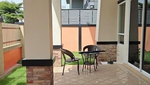 Μια βεράντα με ένα τραπέζι και καρέκλες, έναν πέτρινο τοίχο και θέα σε ένα κτίριο στο βάθος.