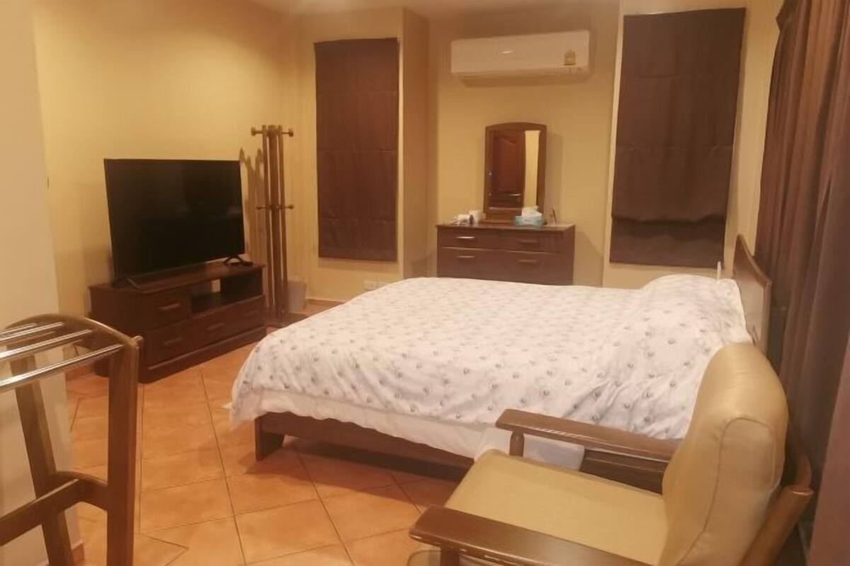 A hotel room with a bed, a TV, a dresser, a mirror, and a window with curtains.