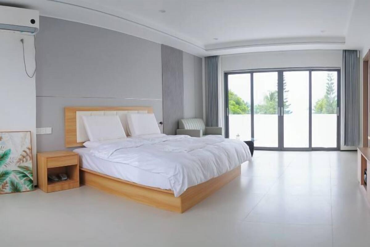 A modern bedroom with a large bed, a bedside table, a chair, and a view of the outdoors through a sliding glass door.