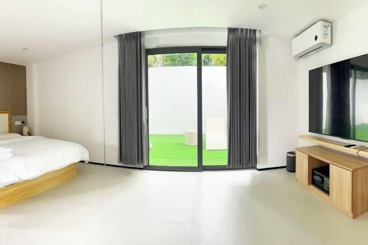 A modern hotel room with a bed, a TV, a sliding door to a balcony, and a built-in TV stand.