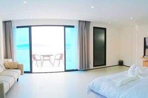A modern hotel room with a large bed, a sofa, a dining area with chairs, and a view of the sea through a glass door. - 1CE HOTEL (Puerto Galera)
