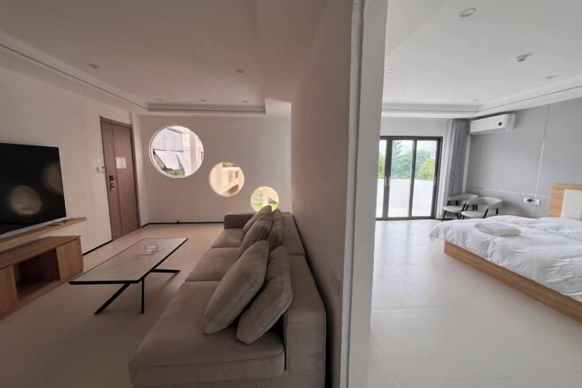 A modern hotel room with a sofa, a TV, a round mirror, and a bed.